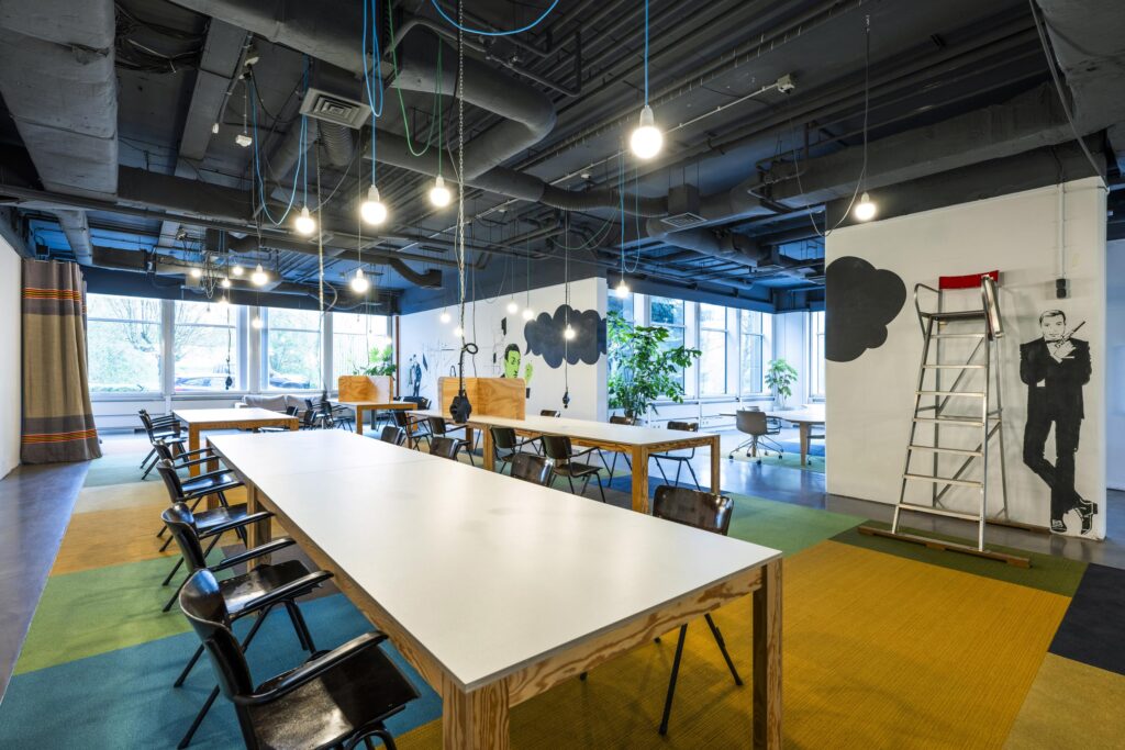 Modern coworking space at Laan van Kronenburg with shared desks, creative wall art, and industrial-style lighting.